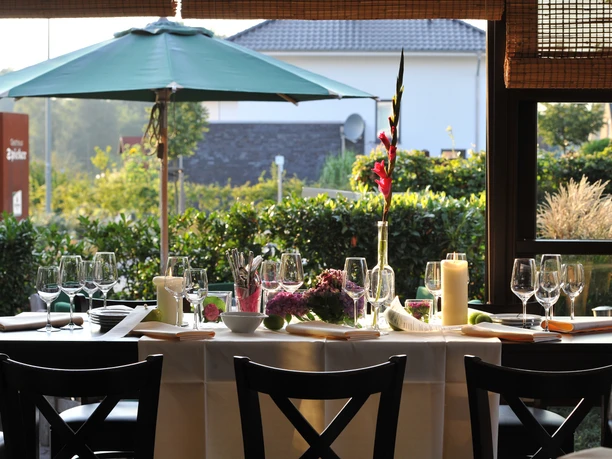 Elegant gedeckter Tisch im Wintergarten, umgeben von Grün, mit Kerzen und festlicher Dekoration.