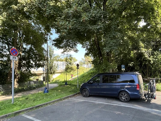 Wohnmobilstellplatz in Mettmann an der Schwarzbachstraße Wohnmobilstellplatz mit einem blauen Fahrzeug im Grünen, umgeben von Bäumen und wenig Verkehr.