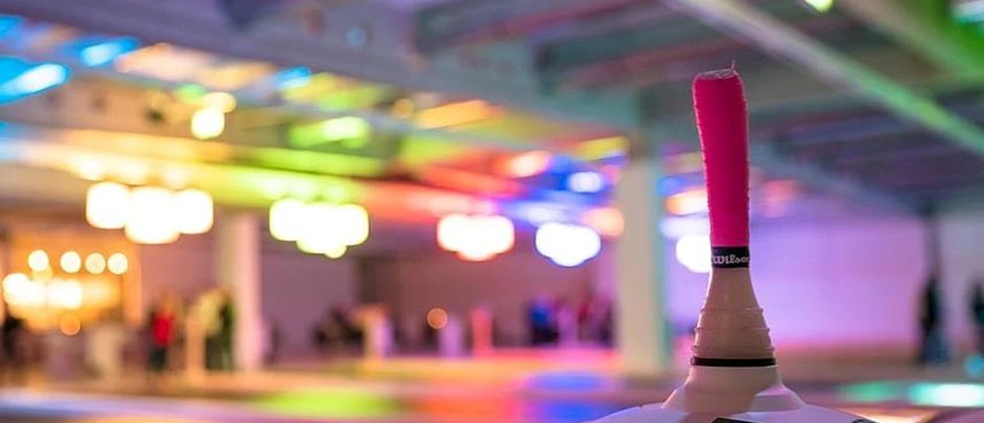 csm_eisspielzeiten-owl_58c81c1c7d.jpg Eine bunte Eishalle mit Besuchern im Hintergrund, im Fokus ein Eisstock mit pinker Griffmanschette.