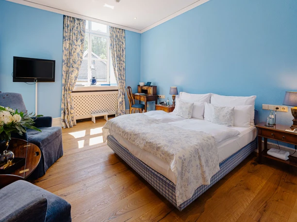Klassisches Doppelzimmer im Schlosshotel Hugenpoet in Essen Doppelzimmer im Schlosshotel Hugenpoet in Essen mit Doppelbett, Holzfußboden und blauen Wänden.