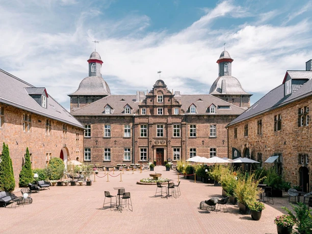 Innenhof vom Schloss Hugenpoet in Essen Historisches Schloss mit Innenhof in Essen, umgeben von Natur, bietet Sitzmöglichkeiten im Freien.