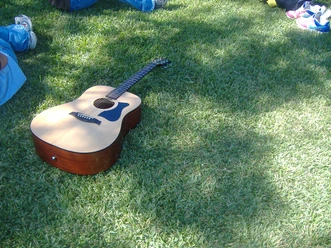 Open Air.jpg Akustische Gitarre liegt auf grünem Gras, umgeben von Personen, von denen nur Beine sichtbar sind