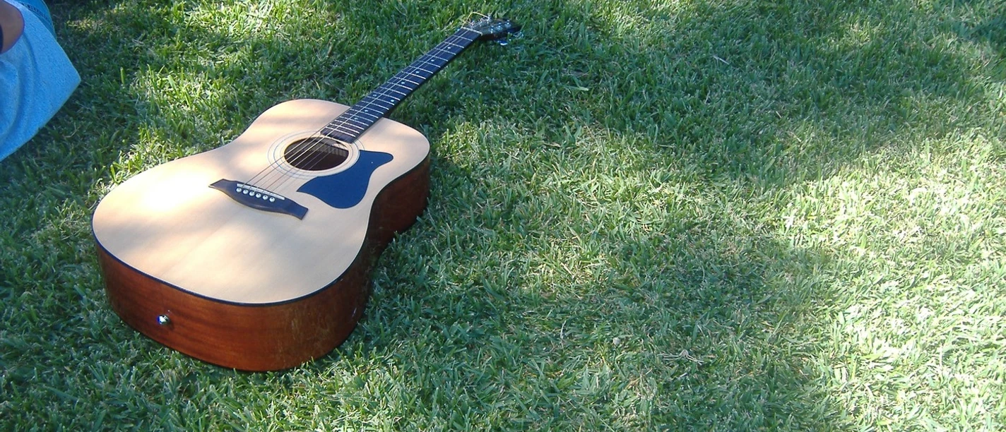 Open Air.jpg Akustische Gitarre liegt auf grünem Gras, umgeben von Personen, von denen nur Beine sichtbar sind