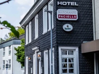 Das Hotel Kimmeskamp und das Ristorante Paciello in Velbert Außenansicht eines dreistöckigen Gebäudes mit dunkler Fassade, Hotel- und Restaurant-Schildern.
