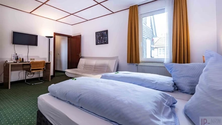 Hotelzimmer im Hotel Kimmeskamp in Velbert Ein helles Hotelzimmer mit einem Doppelbett, einem kleinen Sofa, Schreibtisch und Fenster mit Vorhang.