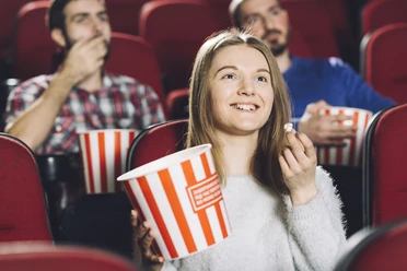Kino-Sessel-Menschen-Popcorn Junge Frau genießt Popcorn mit Freunden in bequemen, roten Kinosesseln. Alle wirken entspannt.