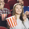 Kino-Sessel-Menschen-Popcorn Junge Frau genießt Popcorn mit Freunden in bequemen, roten Kinosesseln. Alle wirken entspannt.