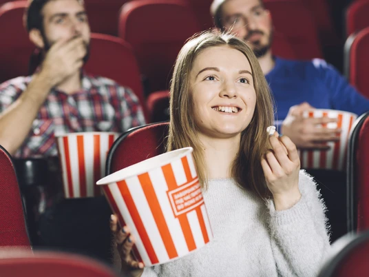 Kino-Sessel-Menschen-Popcorn Junge Frau genießt Popcorn mit Freunden in bequemen, roten Kinosesseln. Alle wirken entspannt.