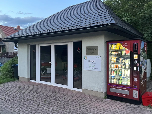 Feuerwehrmuseum Papstdorf mit Proviantomat Kleines Gebäude mit Schieferdach, daneben ein roter Automat mit beleuchteten Flaschen und Snacks.