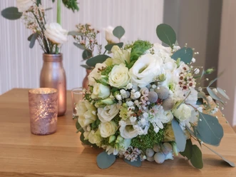 Ein Bouquet aus weißen und grünen Rosen liegt auf einem Holztisch, flankiert von Blumenvasen.