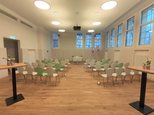 Markthalle_Trausaal_20191218_093317.jpg Trausaal mit modernen, weißen und grünen Stühlen, Holzboden und großen Fenstern, dezente Dekoration.