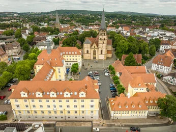 Luftaufnahme des Herforder Rathausplatzes mit Kirche, umgeben von historischen Gebäuden und Bäumen.