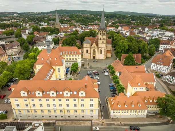 Luftaufnahme des Herforder Rathausplatzes mit Kirche, umgeben von historischen Gebäuden und Bäumen.