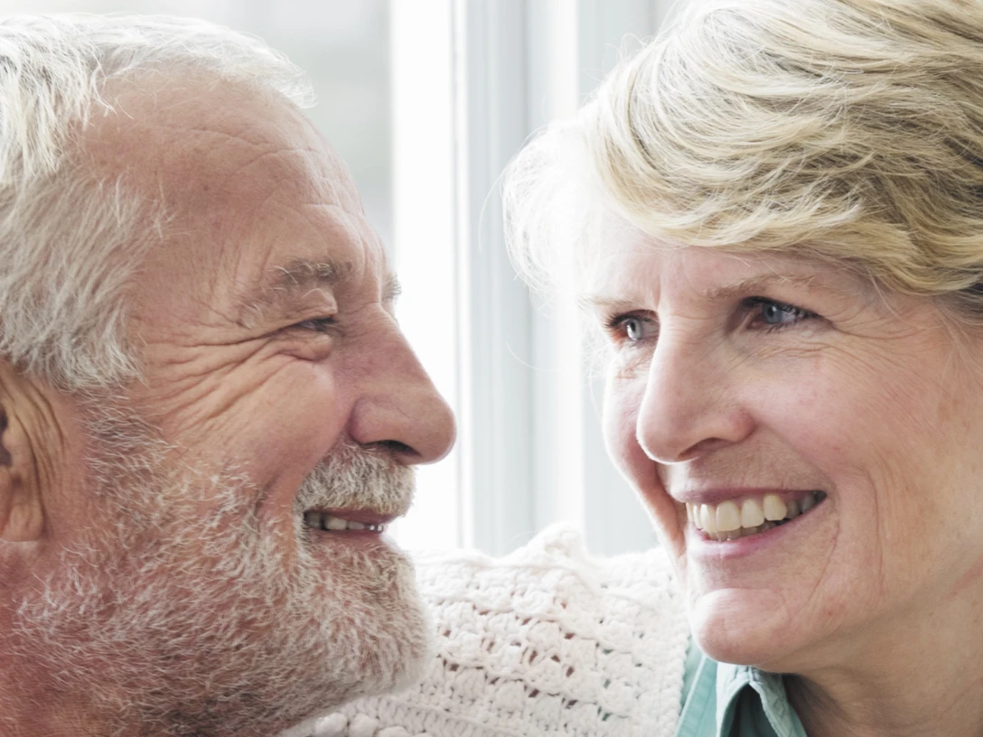 AWO Wohnberatung - Ehepaar.jpg Ein älteres Ehepaar sitzt liebevoll lächelnd nebeneinander, die Frau legt sanft ihre Hand auf den Arm des Mannes.