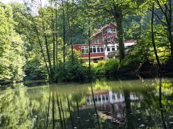 Teich_An den Teichen Rotes Haus am Waldrand spiegelt sich im ruhigen Teich, umgeben von dichtem grünen Laub.A red house on the edge of the forest is reflected in the tranquil pond, surrounded by dense green foliage.Et rødt hus i udkanten af skoven spejler sig i den rolige dam, der er omgivet af tæt, grønt løv.Een rood huis aan de rand van het bos wordt weerspiegeld in de rustige vijver, omringd door dicht groen gebladerte.