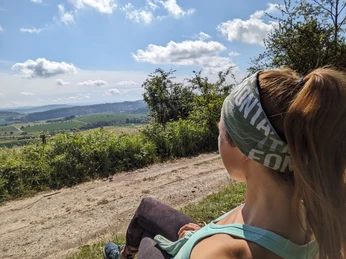 Altendorfer Berg, Wanderkonzept, Fotos, Route Frau sitzt auf Wanderweg am Altendorfer Berg und blickt über grüne Felder und sanfte Hügel.