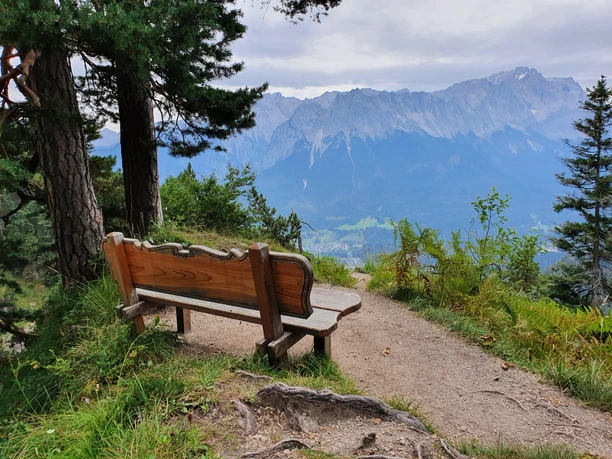 Bank mit Blick zur Zugspitze Holzbank am Bergpfad mit weitem Blick auf bewaldete Hänge und ein markantes Gipfelmassiv