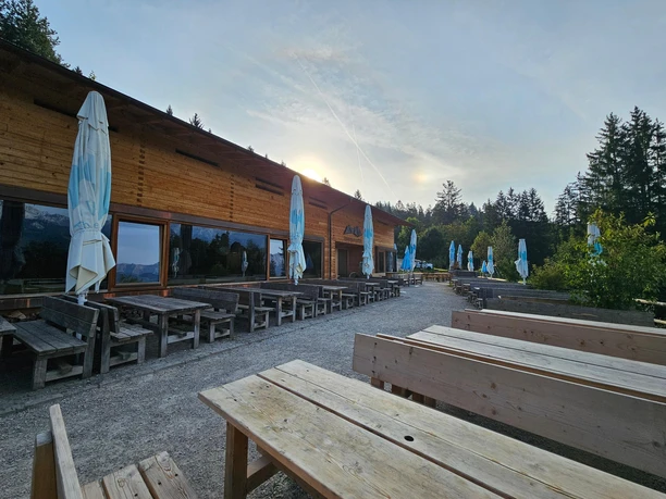 Tannenhütte am Morgen Holzhütte mit leeren Sitzbänken im Morgenlicht, umgeben von Bäumen und leichtem Dunst