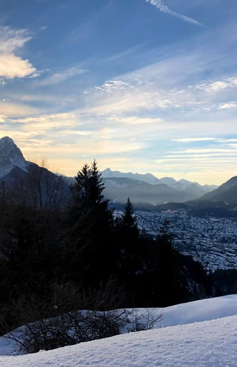 Blick auf Garmisch-Partenkirchen Winterliche Berglandschaft mit Sonnenaufgang über einem Talort und verschneiten Hängen