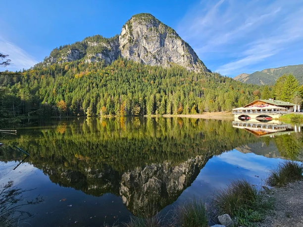 Blick auf den Berggasthof Pflegersee Berggasthof am ruhigen See vor bewaldetem Felsmassiv mit klarer Spiegelung im Wasser
