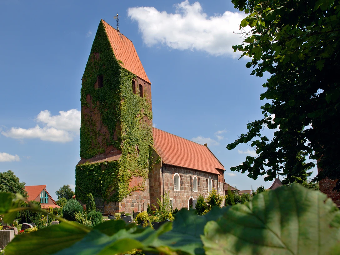 st-johanneskirche Die St.-Johanneskirche mit efeubewachsenem Turm und roten Dächern vor klarblauem Himmel.