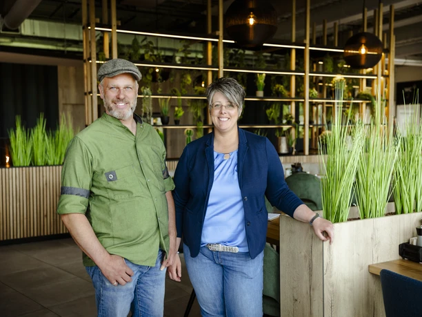 2-Betreiber.jpg Ein Mann und eine Frau lächeln in einem modernen, grün dekorierten Restaurant.