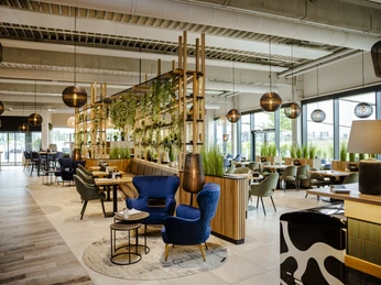 1-Ambiente Innenbereich.jpg Modernes Restaurantinterieur mit blauen Polsterstühlen, hölzernen Trennelementen und stilvollen Lampen.