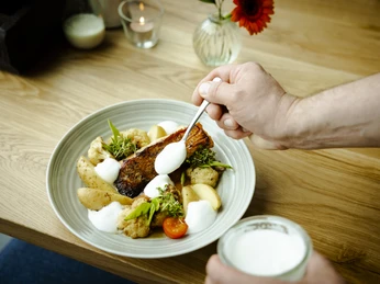 3-Food.jpg Ein Teller mit gebratenem Fisch, Kartoffeln und Gemüse, dekoriert mit weißen Soßenklecksen.