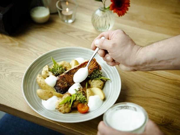3-Food.jpg Ein Teller mit gebratenem Fisch, Kartoffeln und Gemüse, dekoriert mit weißen Soßenklecksen.