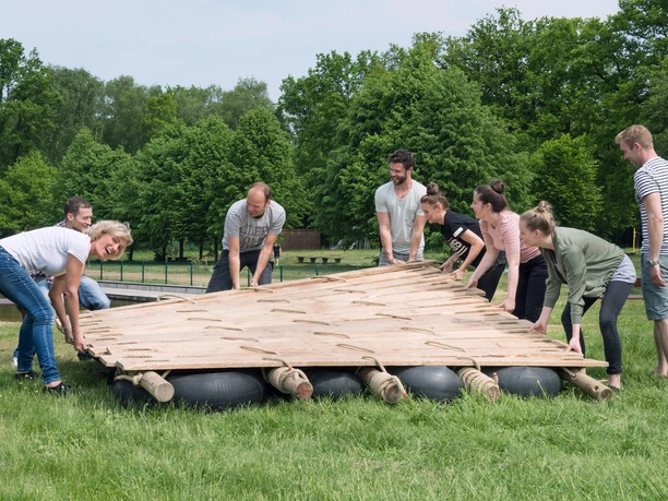 Teamgeist: Floßbau Eine Gruppe hebt ein Floß beim Floßbau-Teamevent der Firma Teamgeist