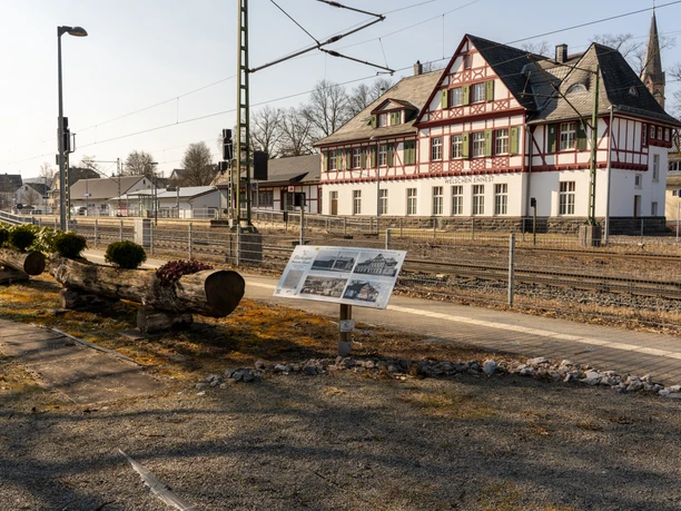 Blickepfad Station 15 - Bahnhof Blick auf das Bahnhofsgebäude in Welschen Ennest. Eine Tafel gibt Wissenswertes zum Gebäude preis.