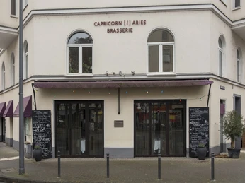 Brasserie Capricorn i aries Ansicht auf die helle Fassade des Restaurants mit zwei Kreidetafeln, die das Menü präsentieren. View of the bright facade of the restaurant with two chalkboards presenting the menu.