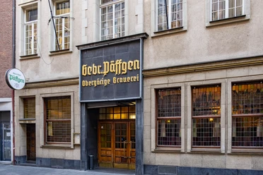 Brewery Päffgen The entrance to the brewery is through a rustic wooden door, with a sign above it decorated with golden letters.