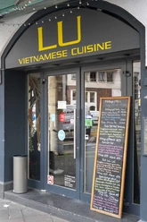 Restaurant LU Vietnamese Eingangsbereich zum Restaurant ist schwarz gestrichen und in gelber Schrift steht der Restaurantname über der Eingangstür. Eine Kreidetafel lehnt an der Hauswand und gibt Einblick auf das Menü.