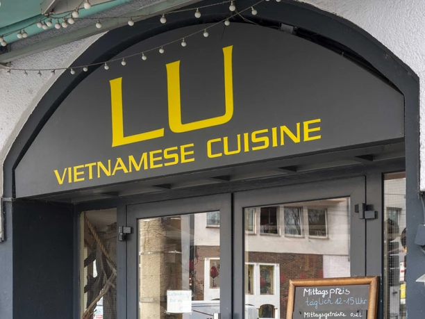 Restaurant LU Vietnamese Eingangsbereich zum Restaurant ist schwarz gestrichen und in gelber Schrift steht der Restaurantname über der Eingangstür. Eine Kreidetafel lehnt an der Hauswand und gibt Einblick auf das Menü.
