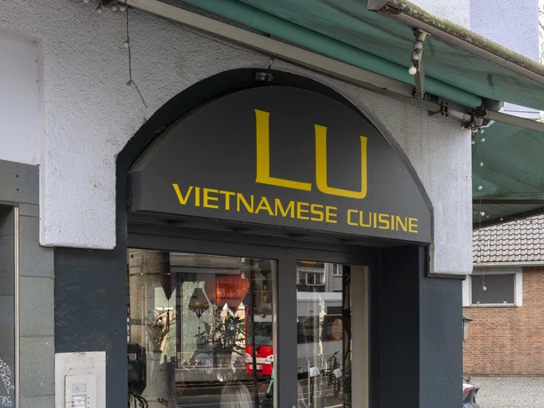 Restaurant LU Vietnamese Blick auf die Hausfassade vom Restaurant. Auf schwarzem Untergrund steht in gelber Schrift der Name und vor der bodentiefen Fensterfront stehen Blumenholzkästen.