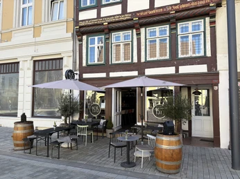 Herford-Weinbar 1575-Hartendorf -Aussenansicht (2).jpeg Außenansicht einer historischen Weinbar mit Fachwerk, Sonnenschirmen und Sitzgelegenheiten im Freien.