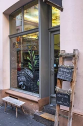 Cafe Hommage Einladendes Fenster mit kleiner Holzbank davor, daneben eine Kreidetafel an einer Holzleiter befestigt.