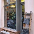 Cafe Hommage Einladendes Fenster mit kleiner Holzbank davor, daneben eine Kreidetafel an einer Holzleiter befestigt.Inviting window with a small wooden bench in front of it, next to it a chalk board attached to a wooden ladder.