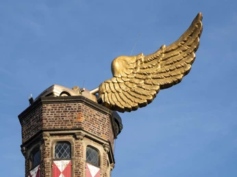 Goldenes Flügelauto Der historische Wehrturm zeigt ein goldenes Flügelauto auf dem Dach, das sich majestätisch in den blauen Himmel erhebt.The historic defense tower features a golden winged car on the roof, which rises majestically into the blue sky.