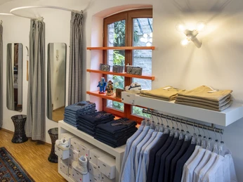 Herrenbude Ein stilvoll eingerichteter Modeladen mit hölzernem Fußboden, in dem ordentlich gefaltete Kleidung und stilvoll platzierte Dekorationen zu sehen sind. Das Bild zeigt einen eleganten Innenraum mit sorgfältig arrangierten Textilien und geschmackvoller Beleuchtung.A stylishly furnished fashion store with a wooden floor showing neatly folded clothes and stylishly placed decorations. The picture shows an elegant interior with carefully arranged textiles and tasteful lighting.