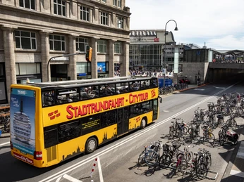 Kölner CityTour Ein markanter, gelber Doppeldeckerbus für Stadtrundfahrten fährt an der Kölner Altstadt vorbei. Zahlreiche Fahrräder stehen in einem eigens dafür vorgesehenen Bereich.A striking yellow double-decker bus for city tours drives past Cologne's old town. Numerous bicycles are parked in a specially designated area.