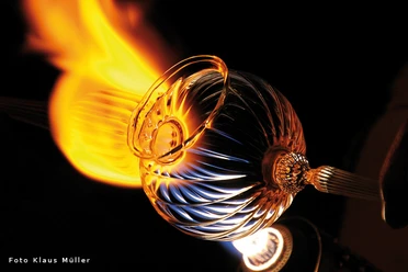 windlicht-live_600.jpg Ein Glasbläser formt ein glühendes, spiralförmig gemustertes Glasobjekt vor Flammenhitze.
