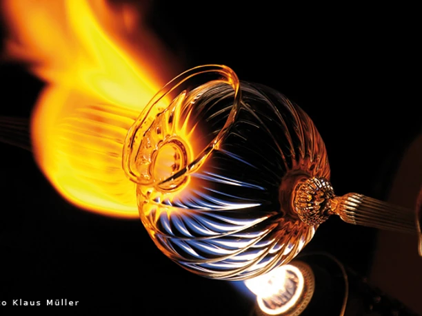 Windlicht Ein Glasbläser formt ein glühendes, spiralförmig gemustertes Glasobjekt vor Flammenhitze.