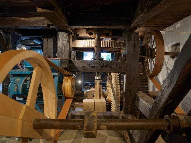 Historische Wassermühle mit komplexen Holzzahnrädern und Mechanismen in einem rustikalen Innenraum.