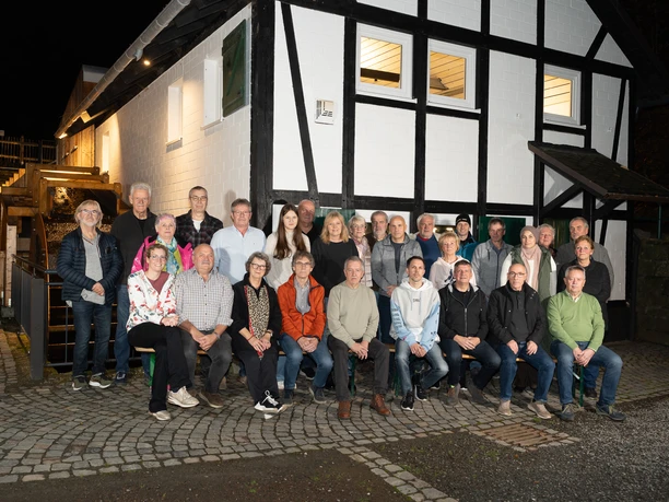 Dümmlinghauser Mühle Eine Gruppe von 32 Personen posiert vor einem weiß-schwarzen Fachwerkhaus auf gepflastertem Boden.