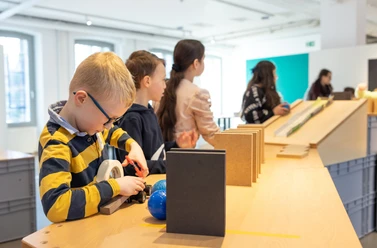 Kettenreaktion für Kinder Kinder beschäftigen sich in einem modernen, lichtdurchfluteten Raum mit interaktiven Stationen.