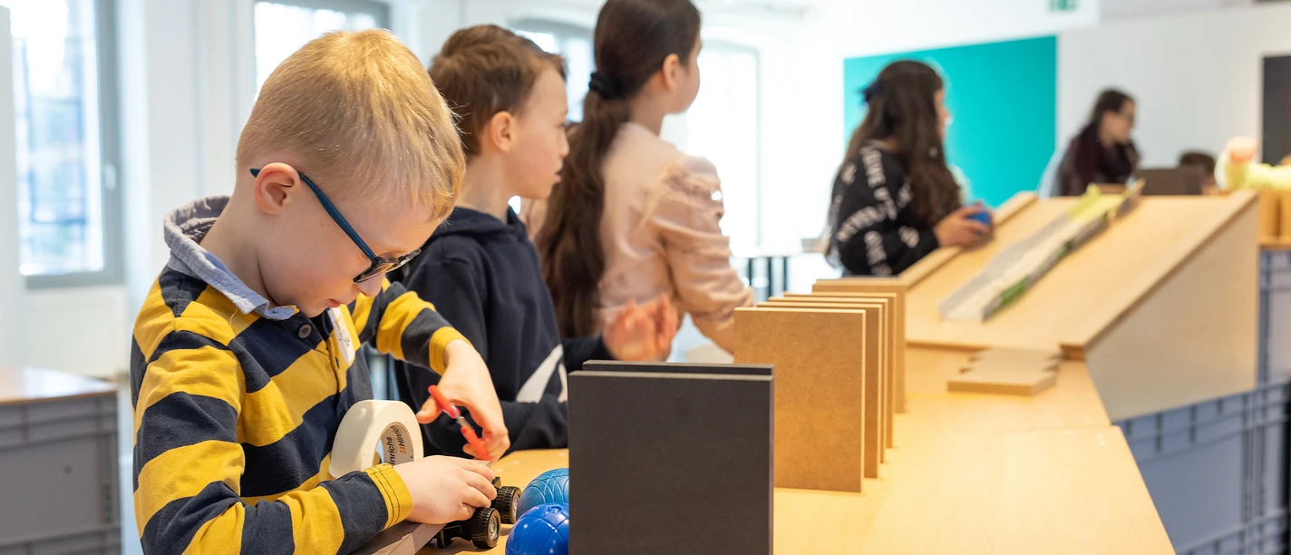 Kettenreaktion für Kinder Kinder beschäftigen sich in einem modernen, lichtdurchfluteten Raum mit interaktiven Stationen.