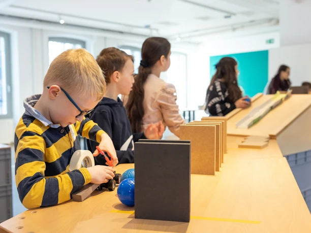 Kettenreaktion für Kinder Kinder beschäftigen sich in einem modernen, lichtdurchfluteten Raum mit interaktiven Stationen.