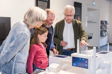 Führung Unter Spannung Eine Gruppe von Erwachsenen und ein Kind betrachten interaktiv ein Miniaturmodell einer Fabrik.